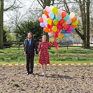 Ein Mann und eine Frau mit einem großen Bündel Luftballons in der Hand auf einem Feld